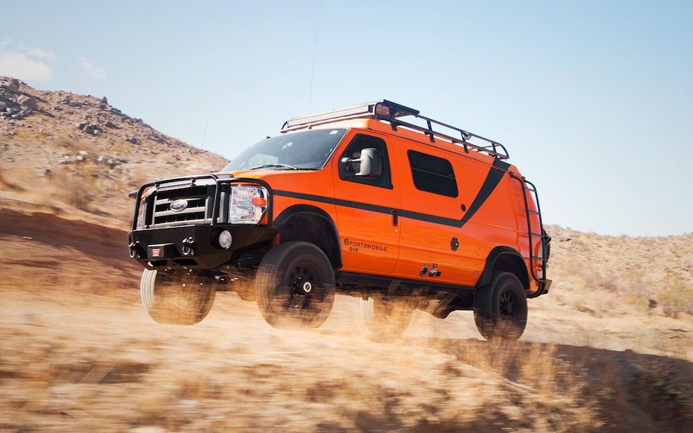 Orange converted Ford van driving through a desert.